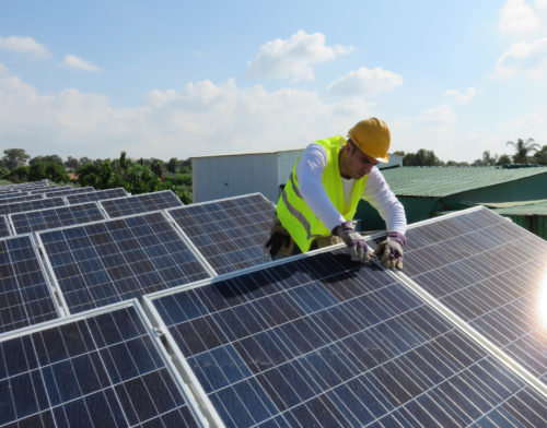 Young maintenance worker installing solar panels on rooftop